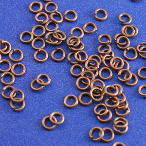 May include: A large quantity of small, copper-colored jump rings. The rings are scattered on a blue surface.