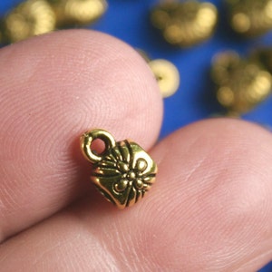 May include: Gold-toned metal end cap with a decorative floral design. The end cap has a small loop at the top for attaching to a cord or string.