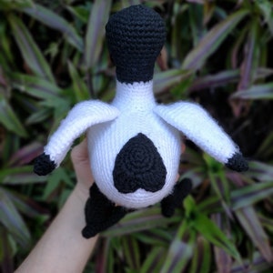 May include: A crocheted stuffed animal in the shape of a bird. The bird is white with black accents, including a black head and a black heart-shaped design on its chest.