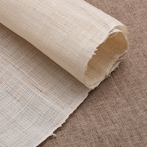May include: A roll of natural white fabric with a woven texture. The fabric is rolled up and the end is visible.
