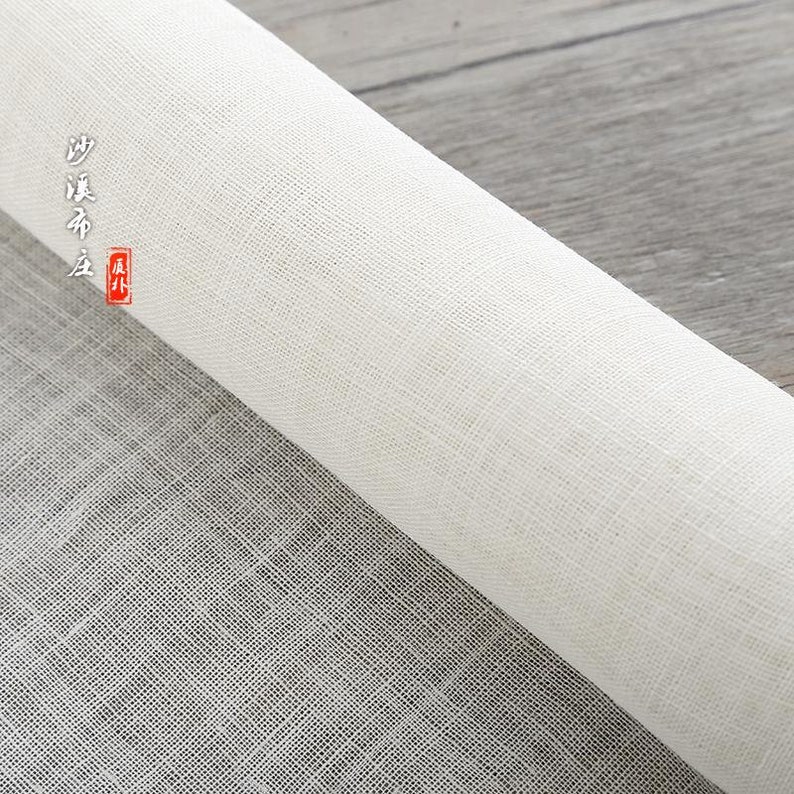 Puede incluir: Un rollo de tela blanca tejida con una textura fina y uniforme. La tela est&aacute; enrollada y el extremo del rollo es visible. La tela est&aacute; etiquetada en caracteres chinos.