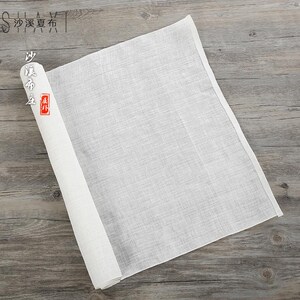Puede incluir: Un trozo de tela blanco rectangular, enrollado sobre una superficie de madera. La tela es lisa y tiene una textura sutil. El texto "沙溪夏布" es visible en la esquina superior izquierda de la imagen.