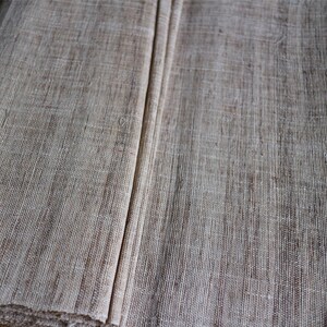 May include: Close-up of a natural woven fabric with a light brown color and a slightly rough texture.