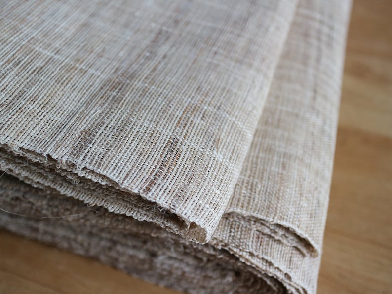 May include: A close-up of a beige woven fabric, folded and rolled up. The fabric has a natural, textured look and feel.