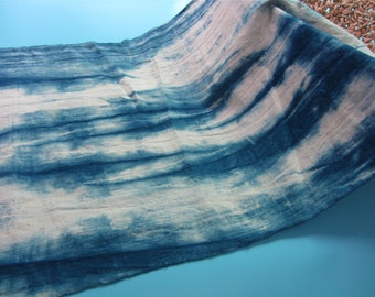 May include: A blue and white tie-dye fabric with a textured surface. The fabric is folded and draped over a blue surface.