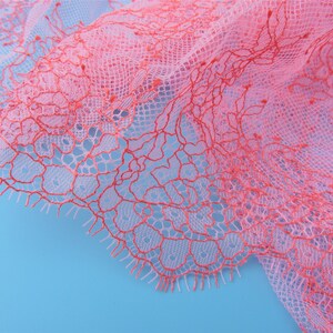 Peut inclure: Tissu de dentelle rose et rouge avec un motif floral d&eacute;licat. La dentelle est douce et transparente, et elle a une surface l&eacute;g&egrave;rement textur&eacute;e.