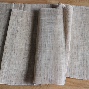 May include: Four beige linen placemats folded and stacked on a wooden surface.