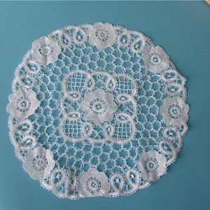 Peut inclure: Napperon en dentelle blanche crochetée avec un motif floral délicat. Le napperon est rond et a un diamètre d'environ 30 cm.