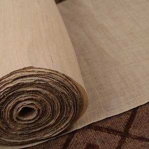 May include: A roll of natural beige fabric, tightly wound and ready to be unrolled. The fabric has a subtle texture and a slightly rough feel.