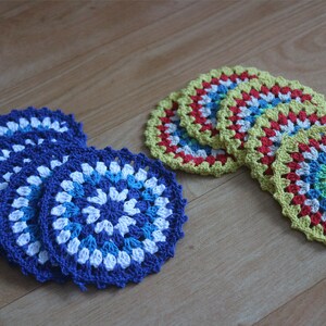 Puede incluir: Conjunto de posavasos de ganchillo en azul, blanco y rojo, y amarillo, rojo y verde. Los posavasos son circulares y tienen un patrón en espiral.