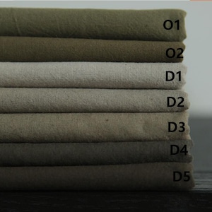 Könnte beinhalten: Ein Stapel von sieben Stoffproben in verschiedenen Grüntönen und Brauntönen. Die Proben sind mit O1, O2, D1, D2, D3, D4 und D5 beschriftet.