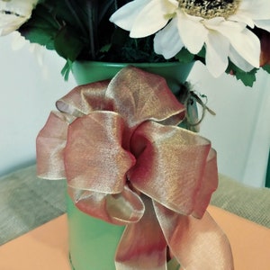 May include: A green metal pitcher with a brown and gold ribbon bow. The pitcher is filled with a bouquet of artificial sunflowers.