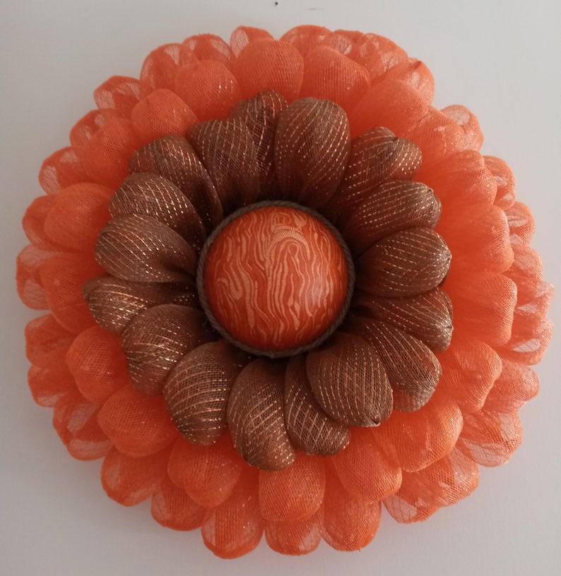 May include: A large orange and brown mesh wreath with a textured orange centre. The wreath is made of multiple layers of mesh and has a rustic, farmhouse style.