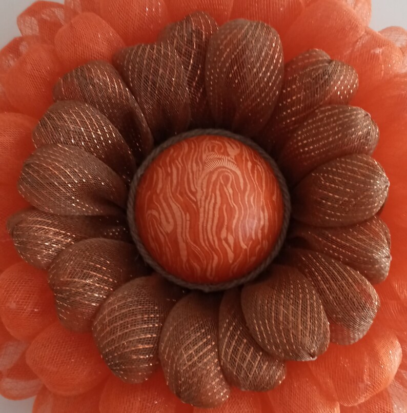 May include: A close-up of a brown and orange wreath with a decorative egg in the centre. The egg has a brown and orange marbled pattern.