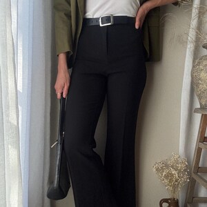 Puede incluir: Una mujer con un blazer verde, una camiseta blanca, pantalones negros y un cintur&oacute;n negro con hebilla plateada. Lleva un bolso negro.