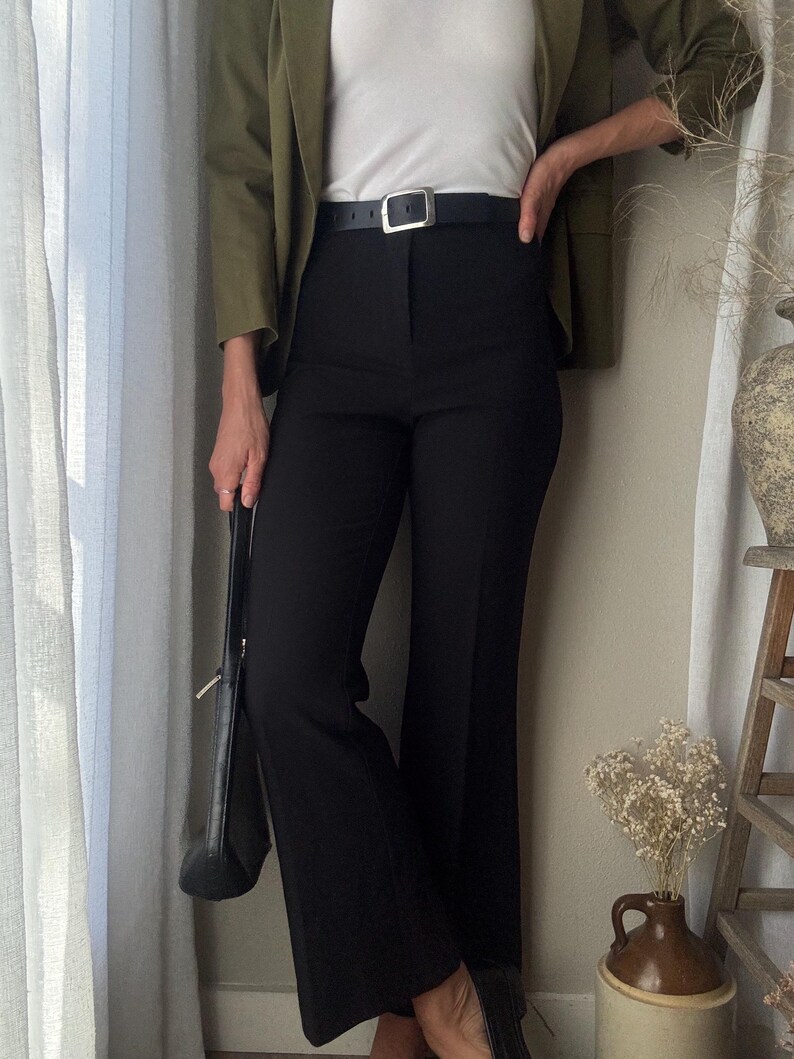 Puede incluir: Una mujer con un blazer verde, una camiseta blanca, pantalones negros y un cintur&oacute;n negro con hebilla plateada. Lleva un bolso negro.