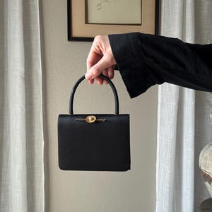 Könnte beinhalten: Eine weiße Keramik-Tasse mit schwarzem Henkel und dem Text "But First, Coffee" in schwarzer, fetter Schrift. Die Tasse steht auf einer weißen Oberfläche. Die Tasse ist etwa 10 cm hoch.