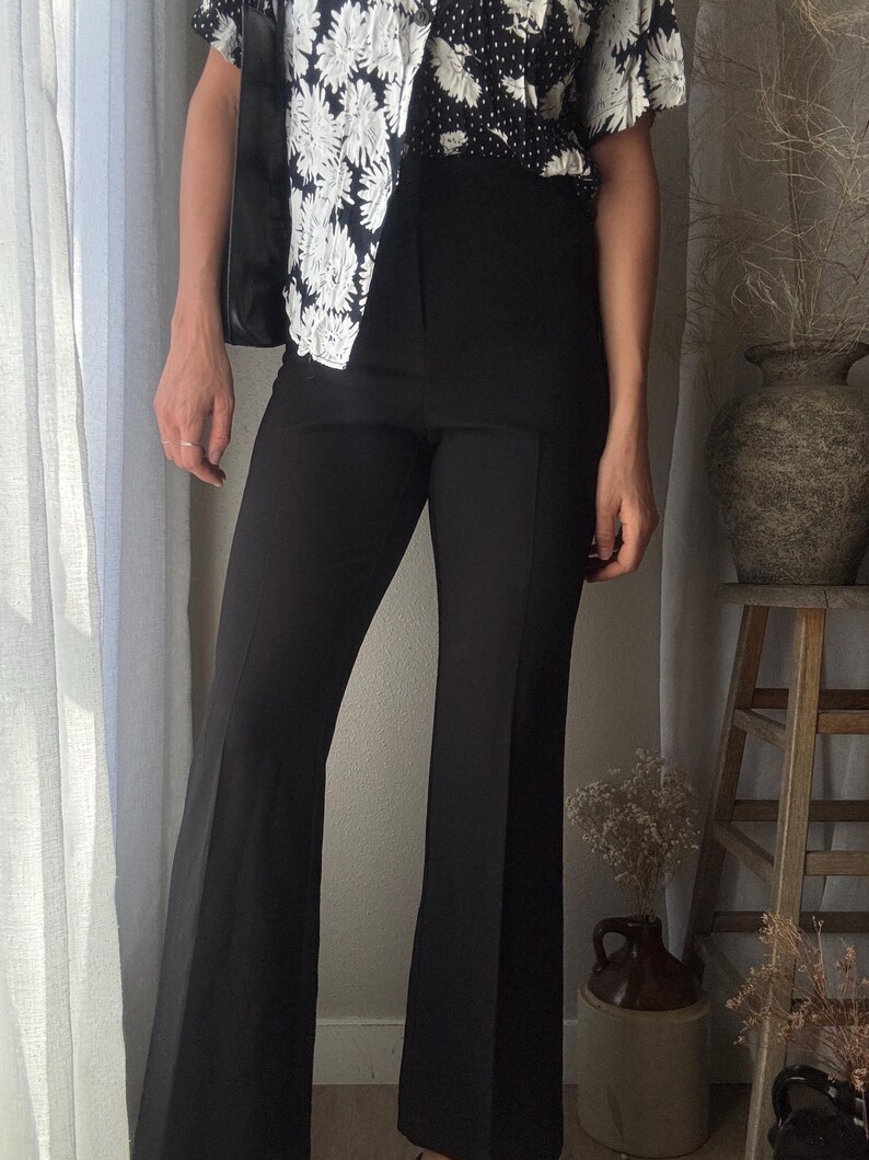 Puede incluir: Pantal&oacute;n negro acampanado de cintura alta. El pantal&oacute;n est&aacute; hecho de una tela lisa y resistente a las arrugas.
