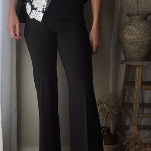 Puede incluir: Una persona que lleva pantalones negros acampanados con una blusa de flores blancas y negras.