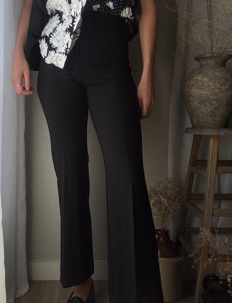 Puede incluir: Una persona que lleva pantalones negros acampanados con una blusa de flores blancas y negras.