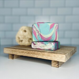 May include: Two bars of handmade soap on a wooden tray. The soap is a swirl of pink, green, and blue with a cactus design.
