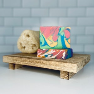 May include: Two bars of colorful swirl soap on a wooden tray. The soap is a mix of pink, yellow, green, and blue.