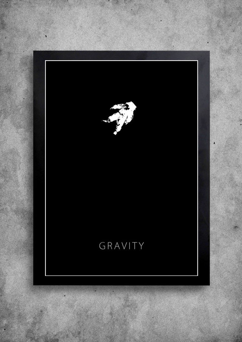 Op de afbeelding: Een minimalistische zwart-wit poster met een wit silhouet van een astronaut die in de ruimte zweeft. De tekst "GRAVITY" is in wit onderaan de poster gedrukt.