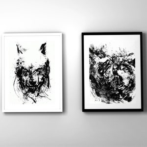 Könnte beinhalten: Zwei gerahmte Schwarzweiß-Tintenzeichnungen von Wolfsgesichtern. Der Wolf links ist in einem weißen Rahmen und der Wolf rechts in einem schwarzen Rahmen.