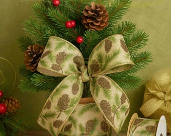 May include: A miniature Christmas tree with green pine needles, red berries, and pine cones. A large bow with a pine cone pattern adorns the tree. A roll of matching ribbon is next to the tree. The theme is holiday decor.