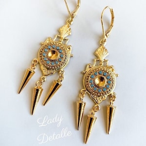 May include: Gold tone earrings with a blue and gold circular design and three gold spikes hanging from each earring.