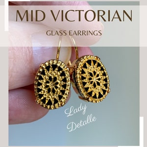 May include: Gold-toned earrings with black glass oval-shaped drops featuring a gold filigree design. The earrings are labeled "Lady Detalle".