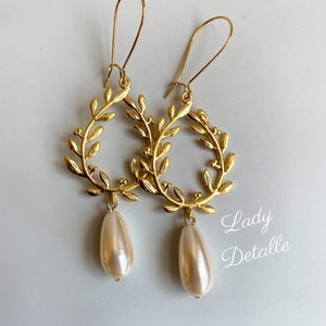 May include: Gold leaf earrings with a pearl drop. The earrings are in the shape of a wreath with small leaves and berries.
