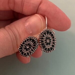 May include: A pair of silver dangle earrings with black oval-shaped charms. The charms have a delicate filigree design.