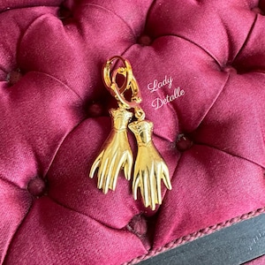K&ouml;nnte beinhalten: Goldene Creolen mit einem baumelnden Handdesign. Die H&auml;nde sind detailliert und haben einen Vintage-Look.