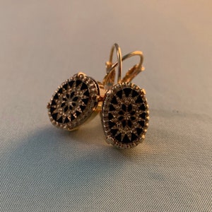May include: A pair of gold-tone earrings with black enamel oval-shaped drop designs. The earrings feature a detailed floral pattern.