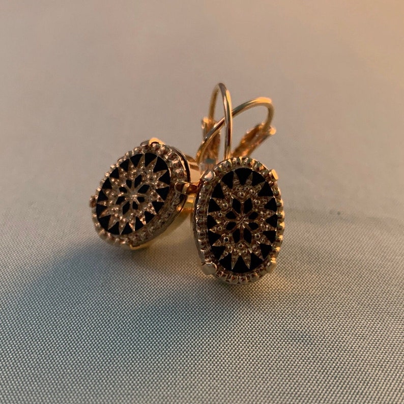 May include: A pair of gold-tone earrings with black enamel oval-shaped drop designs. The earrings feature a detailed floral pattern.