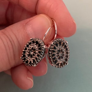 May include: A pair of silver hoop earrings with black oval-shaped stones set in a delicate filigree design.