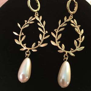 May include: Gold hoop earrings with a delicate leaf design and a dangling pearl drop.