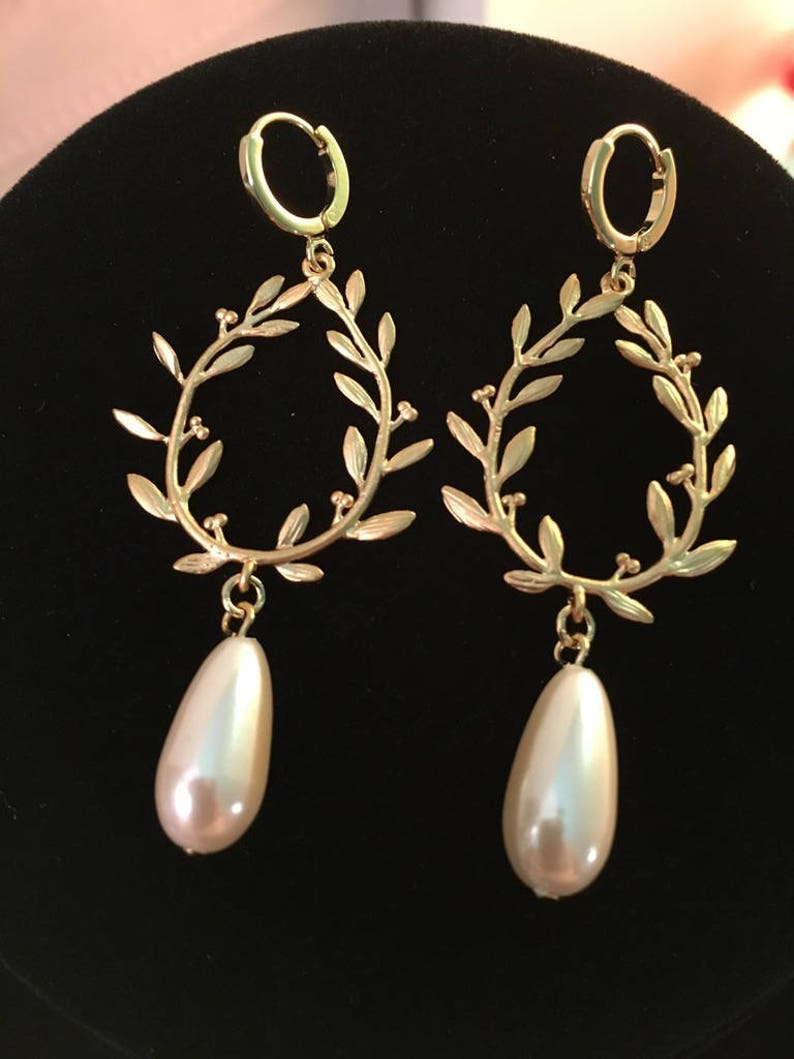 May include: Gold hoop earrings with a delicate leaf design and a dangling pearl drop.