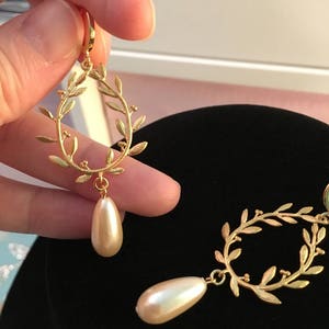May include: Gold tone earrings with a delicate leaf design and a pearlescent drop. The earrings are a classic and elegant style.