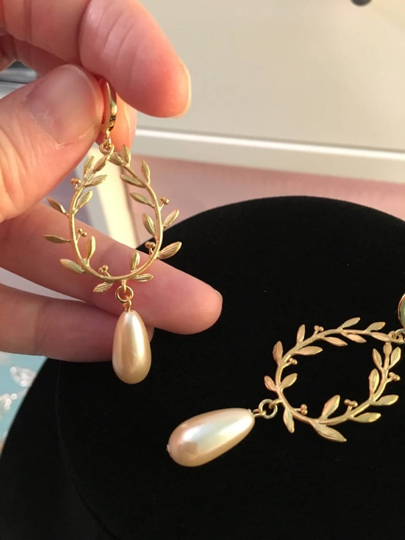 May include: Gold tone earrings with a delicate leaf design and a pearlescent drop. The earrings are a classic and elegant style.