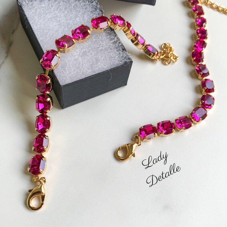 May include: A gold chain bracelet with oval-shaped pink gemstones. The bracelet has two lobster claw clasps.