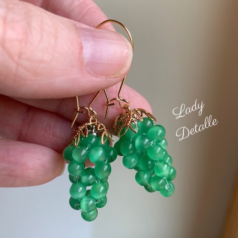 May include: Green glass bead earrings with gold filigree accents. The earrings are shaped like bunches of grapes.