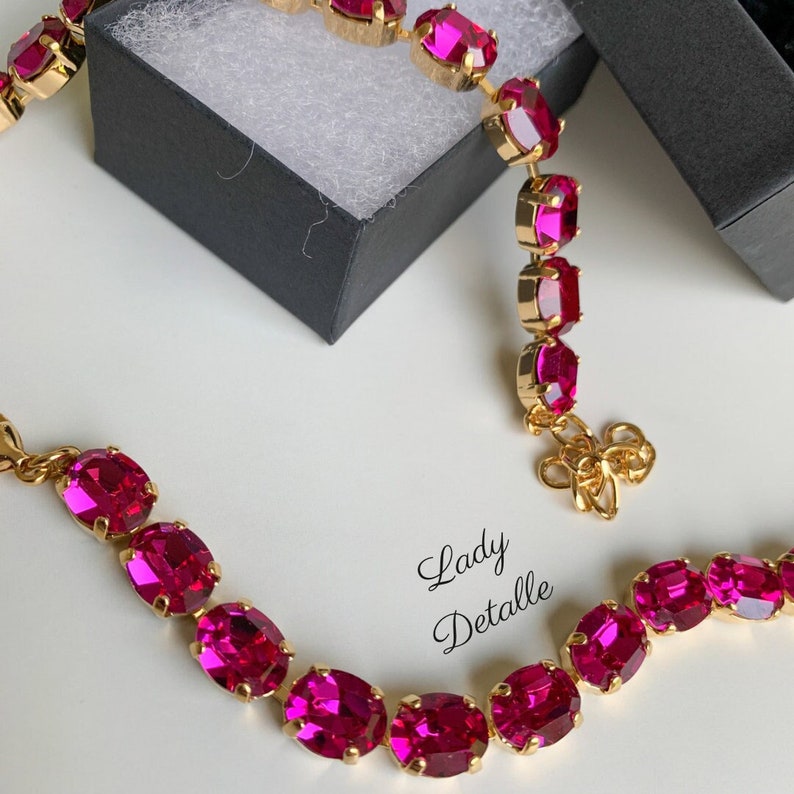 May include: A set of two gold necklaces with oval-shaped pink gemstones. The necklaces are on a white surface with a black box in the background. The text "Lady Detalle" is visible in the image.