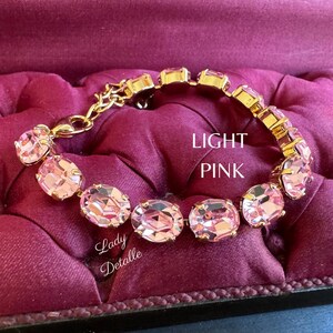 May include: A gold bracelet with light pink oval-shaped crystals. The bracelet is on a pink velvet surface.  LIGHT PINK