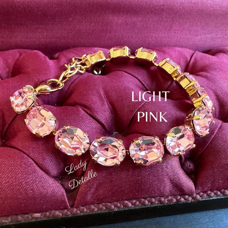May include: A gold bracelet with light pink oval-shaped crystals. The bracelet is on a pink velvet surface.  LIGHT PINK