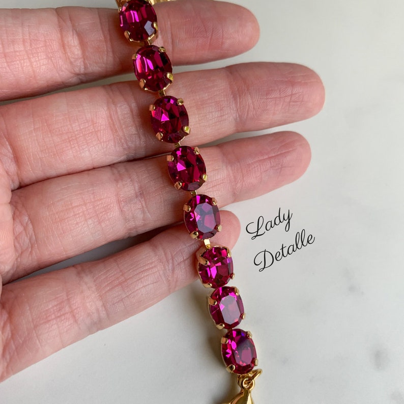 May include: A gold chain bracelet with a row of oval-shaped, fuchsia pink rhinestones.