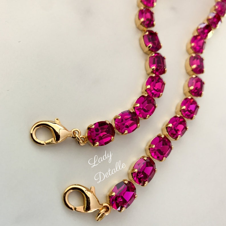 May include: A gold chain bracelet with oval-shaped fuchsia pink rhinestones. The bracelet has two lobster claw clasps.