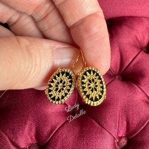 May include: A pair of gold oval earrings with black enamel and a detailed floral design. The earrings have a hook closure.