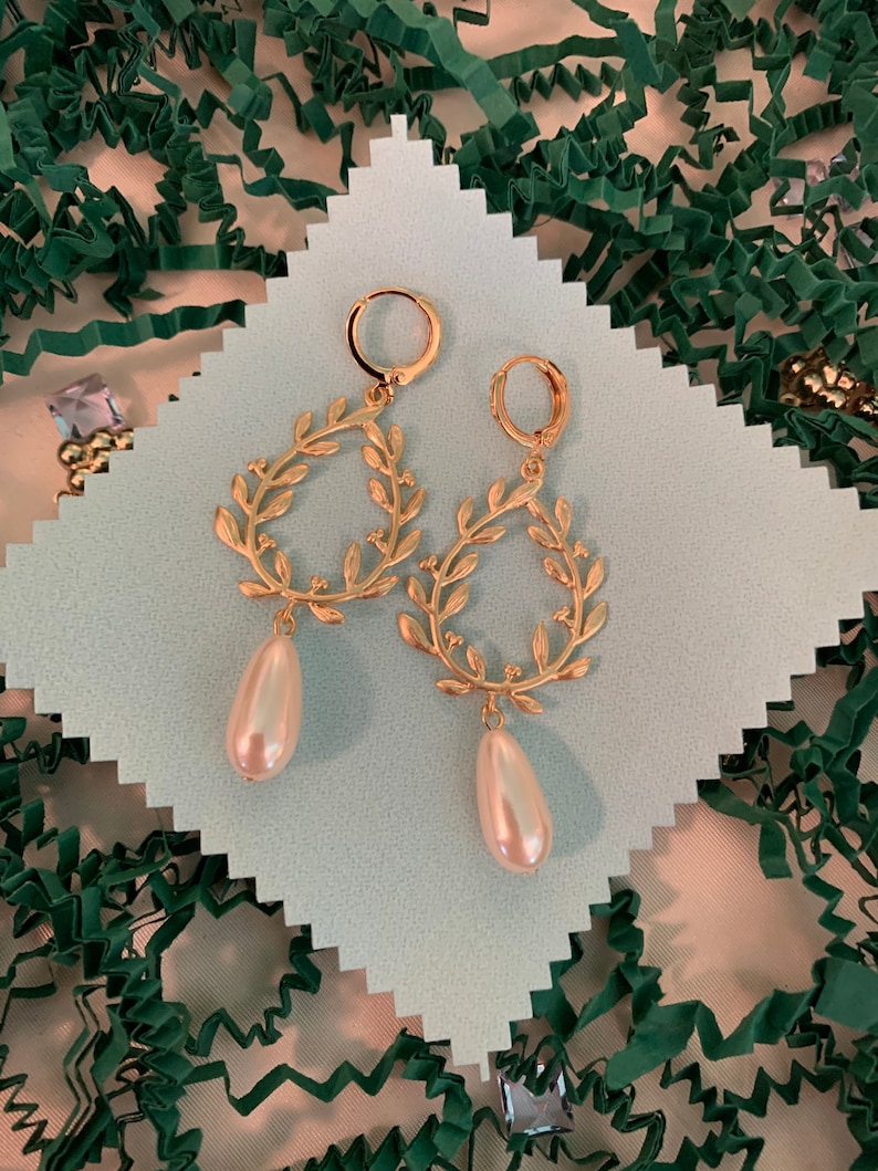 May include: Gold hoop earrings with a delicate leaf design and a dangling pearl drop. The earrings are displayed on a white background.